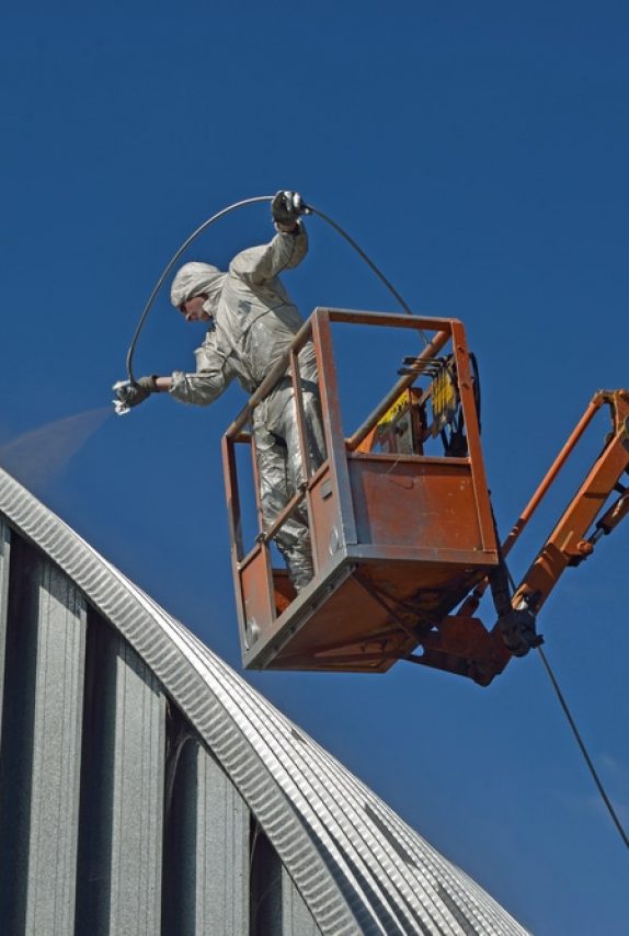 Painter spray painting the roof of a commercial building